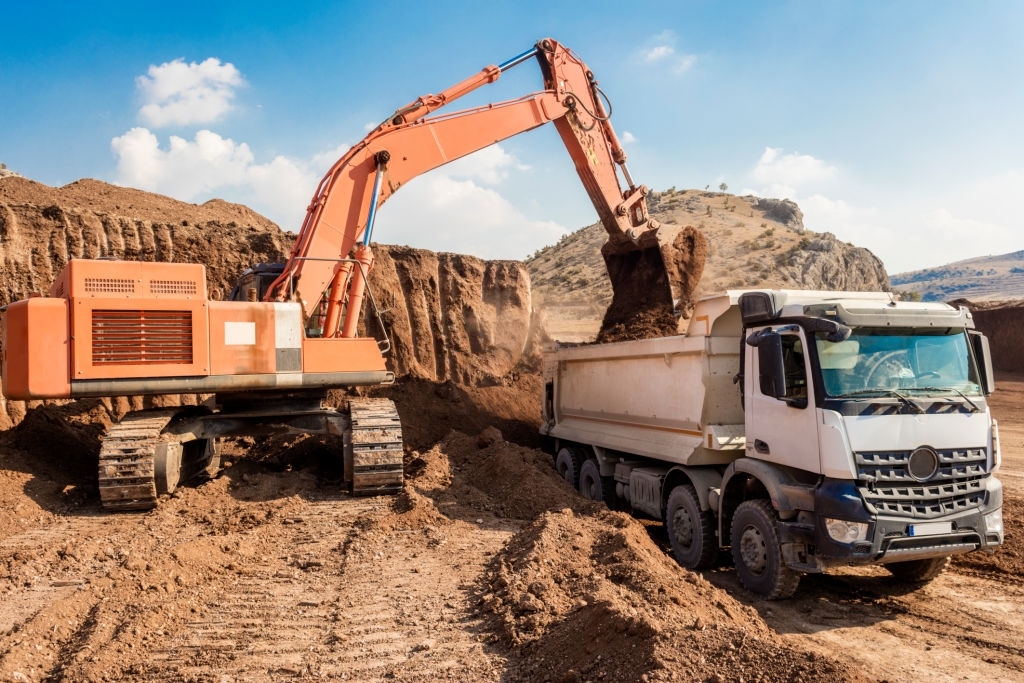 Excavator loading dumper trucks at sunset